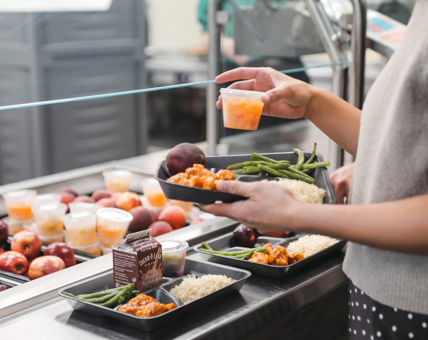 A student grabbing food and placing it on a tray. 